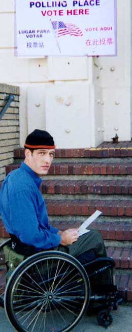 photo of man sitting in wheelchair at bottom of flight of steps to polling site