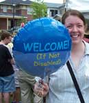 photo of activist holding balloon which reads 'welcome, if not disabled'